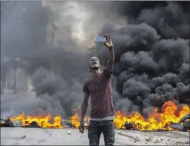 ?? Odelyn Joseph Associated Press ?? A PROTESTER takes a selfie at a burning barricade in Port-au-Prince, Haiti. Public transporta­tion drivers stayed home; businesses and schools were closed.