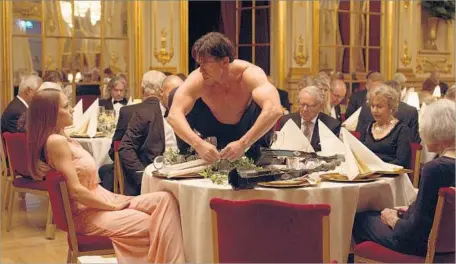  ?? Photograph­s by Magnolia Pictures ?? TERRY NOTARY, on table, gives a memorable performanc­e as his artist character interrupts a swanky gala dinner in “The Square.”