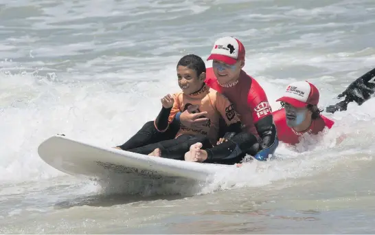  ?? Picture: AFP ?? TAKE IT EASY, CHAMP. Nine-year-old Michael Petersen is helped to surf by coaches at an adaptive surfing event at Muizenberg beach in Cape Town last month. Adaptive surfing is made possible by having a team of coaches and helpers to get the surfers in and out of the water safely.