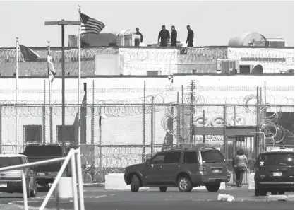  ?? Associated Press ?? People walk on the roof above the front gate of the Great Plains Correction­al Facility on Monday in Hinton, Okla. The GEO Group, Inc., the Florida-based operator of the private prison, estimated that about 400 inmates caused a disturbanc­e late Sunday,...