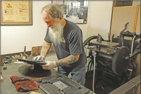  ??  ?? Ackerman cleans the ink plate of the 1890s-era press he uses to print wooden money.