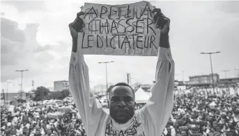  ?? MARCO LONGARI/AFP/GETTY IMAGES ?? A man holds a sign saying “A call to dismiss the dictator” in French in front of a crowd of supporters of the leader of the Cameroonia­n opposition party prior to the Oct. 7 national vote.