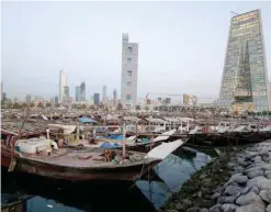  ??  ?? A general view showing fishing vessels docked next to the central fish market in Kuwait City backdroppe­d by the new building of the Central Bank of Kuwait (right).