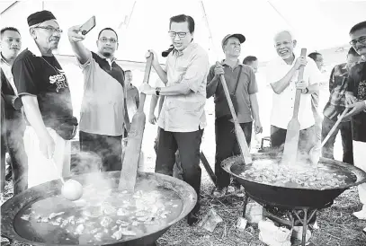  ?? — Gambar Bernama ?? SEPAKAT: Shahrir (dua kanan) bersama Liow (empat kiri) dan penduduk kampung memasak gulai kawah ketika hadir pada Hari Keluarga Felda Lurah Bilut 2018, Bentong semalam.