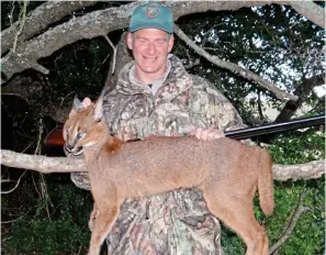  ?? ?? Tragic waste: Known as the desert lynx, the caracal is nocturnal and secretive. British hunter Jim Flowers — thought to have a dozen kills under his belt — clutches this animal’s fur over a tree branch