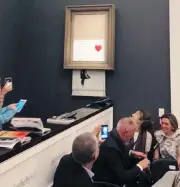  ??  ?? Spectators watch as Girl with Balloon drops through its frame after its auction at Sotheby’s in London. PIERRE KOUKJIAN VIA AP