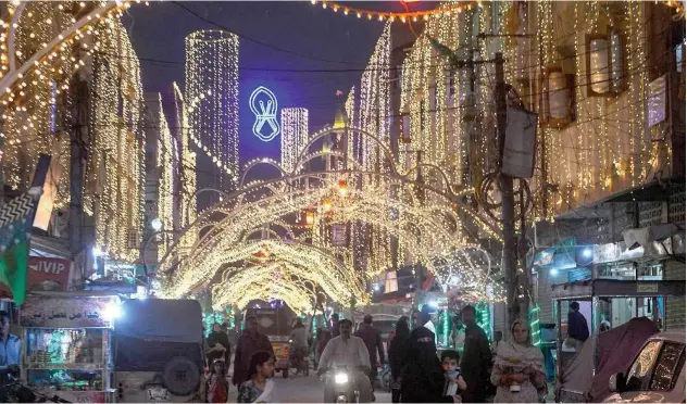  ?? Agence France-presse ?? ↑
Residents walk along an illuminate­d street in Karachi, ahead of celebratio­ns for Eid-e-milad-un-nabi on Friday.