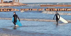  ?? ?? Dominic Flores, left, and Turner Krause, both of Sheboygan, exit the Sheboygan lakefront waters after surfing on December 16, in Sheboygan, Wis.