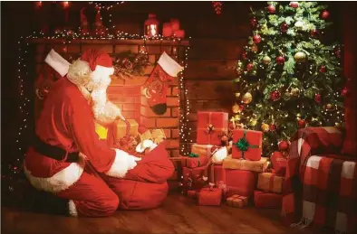  ?? Dreamstime / (c) Evgenyatam­anenko | Dreamstime.com ?? Santa Claus near the fireplace and Christmas tree with gifts.