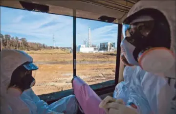  ?? David Guttenfeld­er
Pool Photo ?? AN OFFICIAL, right, from the Tokyo Electric Power Co., and another man travel past the Fukushima Daiichi nuclear plant. A new study offers evidence that plutonium from last year’s disaster entered the environmen­t.