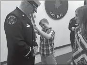  ?? CLAIRE BESSETTE/THE DAY ?? Matthew Manke, 9, struggles to pin the new lieutenant’s badge on his father, Jacob Manke, while the boy’s sister, Leah, 13, looks on during Manke’s promotion ceremony Friday at Norwich Fire Department.