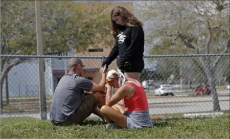  ?? GERALD HERBERT — THE ASSOCIATED PRESS ?? A family prays outside Marjory Stoneman Douglas High School in Parkland, Fla., Sunday. Authoritie­s opened the streets around the school, which had been closed since a mass shooting on Wednesday. Nikolas Cruz, a former student, was charged with 17...