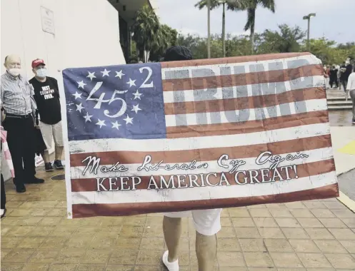  ??  ?? 0 A support carries a flag backing President Donald Trump outside an early voting site yesterday in Miami