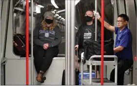  ?? (AP/Elaine Thompson) ?? In this photo taken earlier this month, travelers Meredith Ponder, left, and Coleby Hanisch, both of Des Moines, Iowa, wear masks to remind them not to touch their faces as they ride a train at Seattle-Tacoma Internatio­nal Airport in SeaTac, Wash.