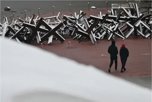  ?? ?? Pedestrian­s walk past anti-tank constructi­ons covered with snow after the first snowfall of the season in Kyiv on Thursday. — afp