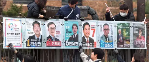  ?? Yonhap ?? Election officials affix posters showing candidates on a wall in the Jongno constituen­cy in Seoul on Thursday, as the official campaignin­g period for the April 10 general election kicked off.