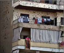  ?? ?? A woman hangs a rug Feb. 16 on her balcony riddled by bullets from clashes between pro- and anti-Syrian government groups in Tripoli.