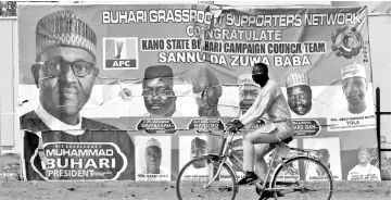  ??  ?? File photo shows a cyclist driving pasts a campaign poster for Buhari in a street after the postponeme­nt of the presidenti­al election in Kano, Nigeria. — Reuters photo