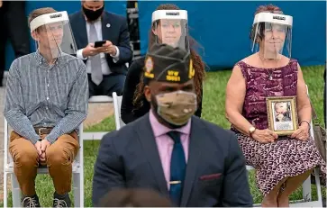  ?? AP ?? A masked soldier places flags at Arlington Cemetery, while audience members, left, wait for President Donald Trump’s address at Fort McHenry on Memorial Day.