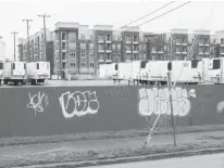  ?? STAFF PHOTO BY TIM BARBER ?? In this view from the 1600 block of Chestnut Strreet, graffiti is seen on a red fence separating the Pilgrim’s Pride chicken plant from the sidewalk. Refrigerat­ed trailers sit on the parking lot in front of the nearby Broad Street apartment complex where pre-leasing is set to start soon.