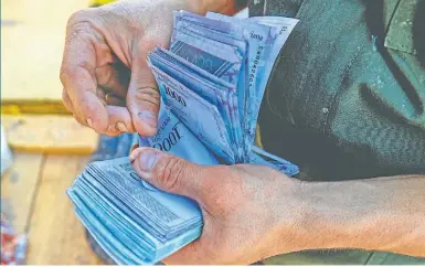  ?? AFP/FEDERICO PARRA ?? A man counts 1,000-bolívar-bills to buy groceries at the municipal market of Coche, a neighbourh­ood of Caracas. According to an IMF projection that poses volatile scenarios, inflation in Venezuela would reach 1,000,000 percent this year, with a single...