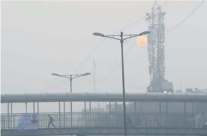  ?? Associated Press ?? A schoolboy walks across a pedestrian bridge as the morning sun is enveloped by a blanket of smog in New Delhi on Tuesday.