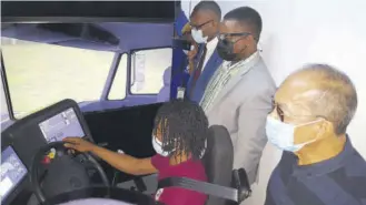  ?? (Photo: Philp Lemonte) ?? A student (seated) enrolled in the Articulate­d Truck Driving Programme at the Caribbean Military Technical Training Institute (CMTTI) Western Campus in Flanker demonstrat­es driving lessons with the use of a simulator to (from left) Minister of Security Dr Horace Chang, and Members parliament Heroy Clarke and Morland Wilson last week.