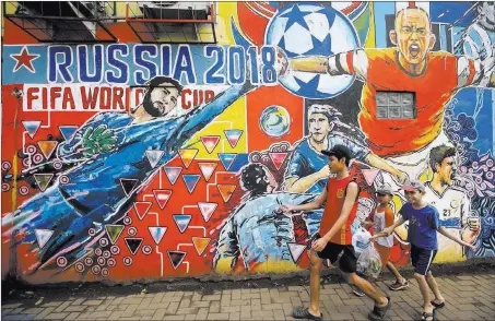  ?? Tatan Syuflana ?? Boys walk Tuesday past a mural on the outskirts of Jakarta, Indonesia, advertisin­g the 2018 World Cup soccer tournament. The Associated Press