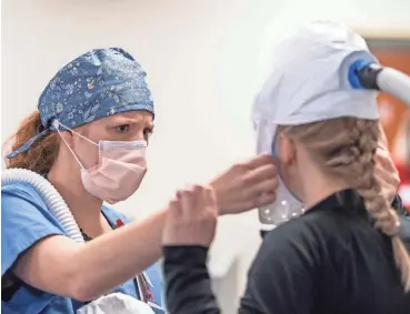  ?? COURTESY OF COREY WILSON ?? Amanda Nienow, a former registered nurse at Bellin Health, assists Hailey McGlin, a certified nursing assistant, in adjusting the hood of a powered air-purifying respirator at Bellin Hospital in Green Bay last fall.