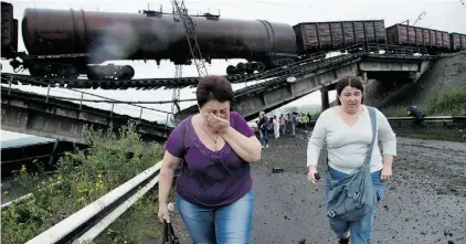  ?? Dmitry Lovetsky/The Associated Press ?? People walk under a railroad bridge destroyed by pro-Russian forces north of Donetsk in Ukraine on Monday.