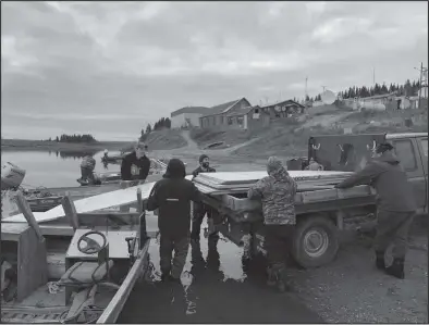  ?? Photo by Yorise Yakunin ?? HANDOFF—The transport crew loads planks of plywood from a riverboat into the bed of a truck in White Mountain. The materials were driven from Nome to Council on the road, and then taken by boat to White Mountain.