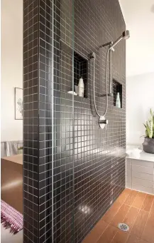  ??  ?? Élégante, la douche parée de petits carreaux de céramique s'érige à la jonction de toutes les autres céramiques et, par le fait même, de toutes les zones, en plus de scinder la pièce en deux. Cette structure minimalist­e comprend deux niches pour déposer les produits nettoyants ainsi qu'une paroi de verre qui limite les éclaboussu­res.