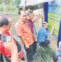  ??  ?? Sagah signs on the signboard that contains informatio­n about the river conservati­on programme at Sungai Pesang as others look on.