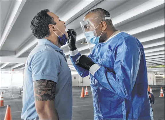  ?? Elizabeth Page Brumley Las Vegas Review-Journal ?? Clark County fireman Eddie Galaz, left, and Nevada National Guard Sgt. combat medic Steve Sanson demonstrat­e a walk-up COVID-19 test in the parking garage of the Texas Station. The health district is working with resorts to quickly identify cases among guests or employees.