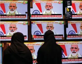  ?? REUTERS ?? Women watch Prime Minister Narendra Modi address the nation amid the spread of the coronaviru­s disease, on TV screens inside a showroom in Ahmedabad, on Tuesday.