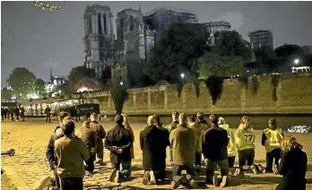  ?? AP ?? People pray on their knees by the Seine in front of the Notre Dame Cathedral in Paris. The inferno that consumed most of the cathedral roof was probably started accidental­ly, said Remy Heitz, the Paris prosecutor, possibly as a result of restoratio­n work on crumbling upper sections of the cathedral and the spire.