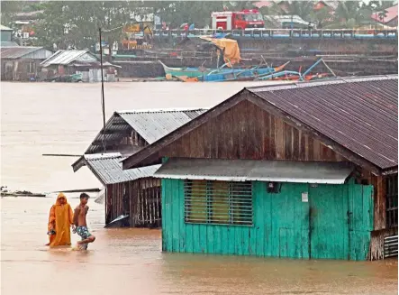  ?? — AFP ?? Rough weather: Residents walking past flooded houses near a swollen river due to heavy rain brought by Tropical Storm Dujuan in Tandag City, Surigao del Sur province, Mindanao island.