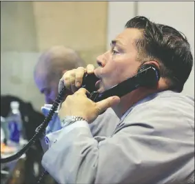  ?? AP Photo/RICHARD DREW ?? A trader uses a pair of telephones Friday as he works in his post on the floor of the New York Stock Exchange. U.S. stocks opened higher, seeking their first gain this week, as beaten-down energy and financial companies rebounded.