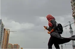  ?? Photo by Shihab ?? A resident struggles to walk in the windy weather during the overcast morning, which also created hazy conditions. —