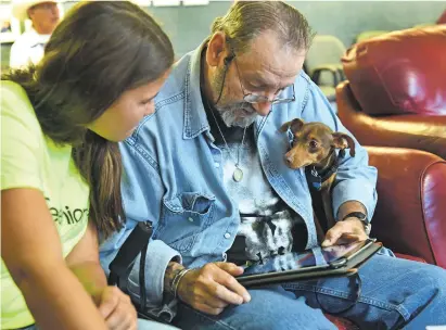  ?? CLYDE MUELLER/THE NEW MEXICAN ?? From left, Kaitlyn Ackros of Albuquerqu­e helps Charles Jones of Santa Fe and his dog, Sunny, register Sunny’s microchip online Thursday at the Alto Street Senior Care Center. The ‘Teeniors’ earn between $10 and $15 an hour teaching elderly people how...