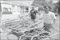  ??  ?? Volunteers Ron Hicks (left) and Magnolia Scullark pile debris into a wheelbarro­w in front of the center where a newly constructe­d outdoor deck and handicap ramp were damaged.