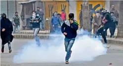  ?? — PTI ?? Youths throw stones on police amid tear gas smoke fired by police to disperse them during clashes between police and protesters,who were protesting in support of demand for the return of mortal remains of JKLF founder Maqbool Bhat on his 34th hanging...