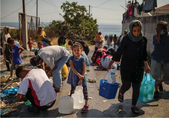  ?? FOTO: ANGELOS TZORTZINIS/LEHTIKUVA-AFP ?? En flicka väntar på att få fylla sin vattenflas­ka vid vägrenen på Lesbos östkust. Hon liksom 12 000 andra blev hemlösa när Moria brann ned.