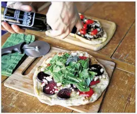  ?? TINA PHAN / AMERICAN-STATESMAN ?? Statesman food writerAddi­e Broyles garnishes a beet, feta cheese and greens grilled pizza with some olive oil. Broyles prepared the pizza on a grill in the backyard of her home.