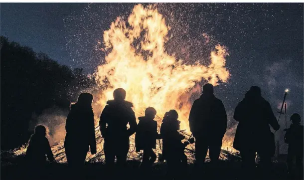  ?? FOTO: BORIS ROESSLER/DPA ?? Menschen stehen an einem traditione­llen Osterfeuer.