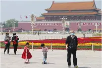  ?? (China Daily via Reuters) ?? PEOPLE WEARING face masks walk past flower installati­ons yesterday at Tiananmen Square in Beijing.