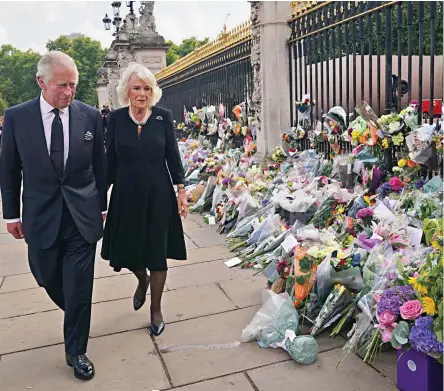  ?? ?? Touching tribute: King Charles and Camilla walk past flowers laid outside Buckingham Palace yesterday