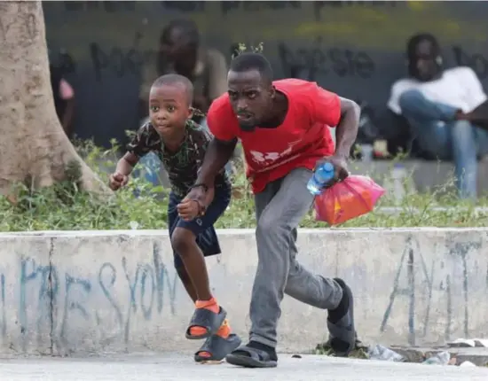  ?? © Ralph Tedy Erol/reuters ?? Een man en een kind vluchten weg voor geweerscho­ten in de hoofdstad Port-au-Prince, op 21 maart.