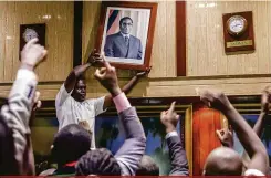  ?? Jekessai Njkizan/AFP ?? Populares que acompanhav­am a sessão do Parlamento retiram o retrato do ex-presidente Robert Mugabe