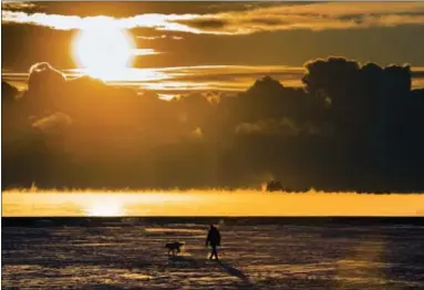  ?? FRANK GUNN — THE CANADIAN PRESS VIA ASSOCIATED PRESS ?? On Dec. 27, 2017, a man walks his dog across the snow-covered beach while a cargo ship sits in the steaming fog of Lake Ontario in Toronto. According to a report released on Thursday, U.S. and British scientists calculate that 2017 wasn’t the hottest...